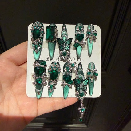 Handmade Emerald Green Cat Eye Long Stiletto Press On Nails. Luxury witchy false nails decorated with 3D green butterfly charms, large emerald crystals, pearls, silver rhinestones and dangling gem chains. Reusable fake nails for parties and cosplay.