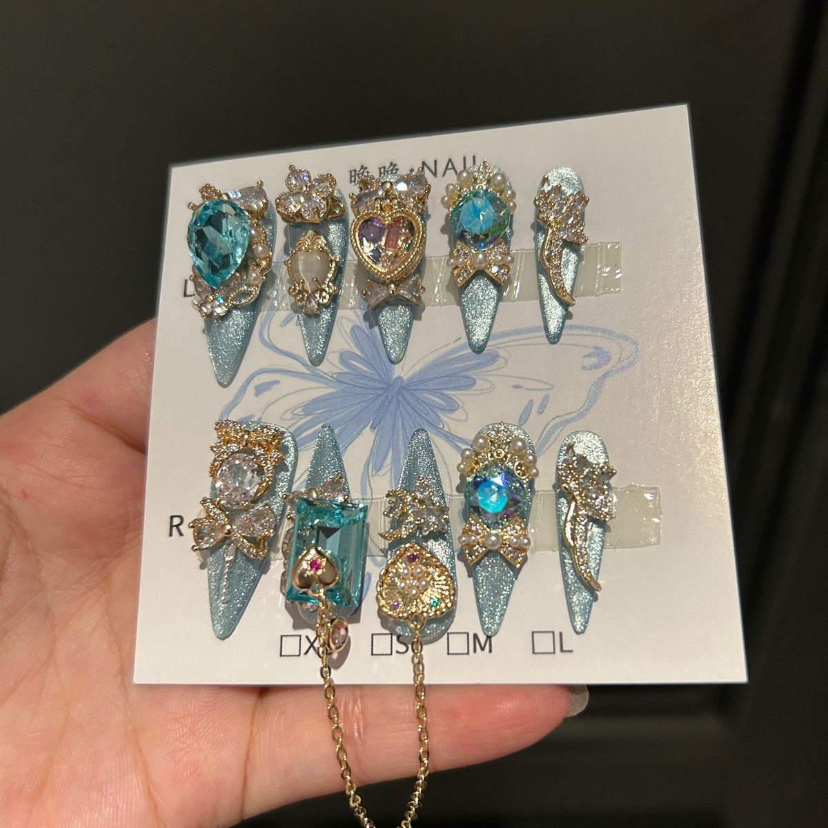 Silver Blue Cat Eye Stiletto Press-on Nails with Over-sized Blue Crystal Gems, Gold Bow, and Interlinked Hanging Chain - Luxury Glam Fake Nail Set