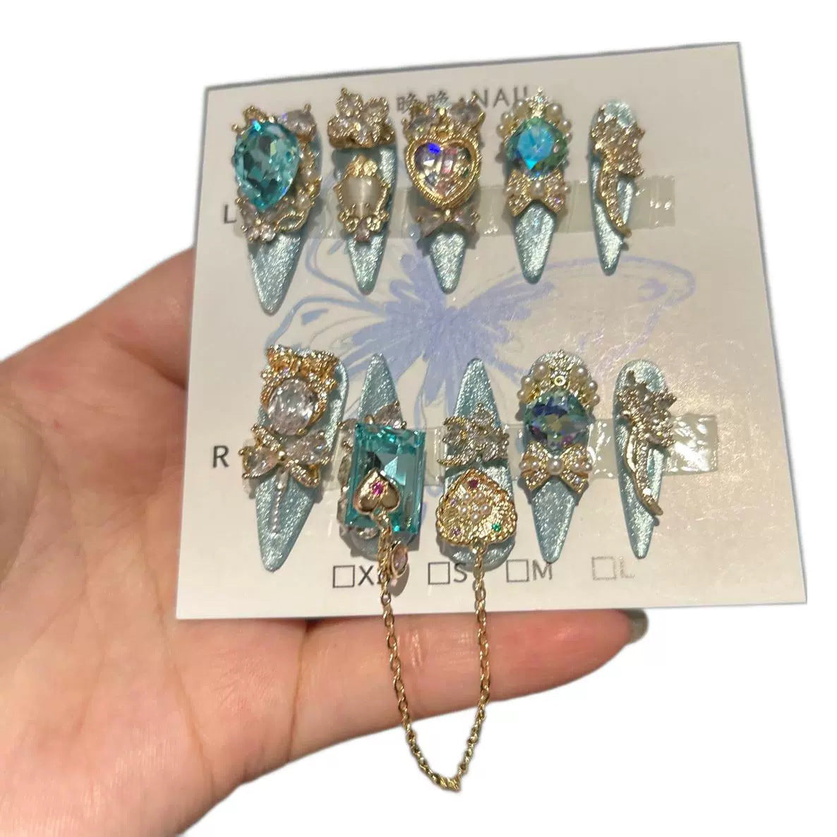 Silver Blue Cat Eye Stiletto Press-on Nails with Over-sized Blue Crystal Gems, Gold Bow, and Interlinked Hanging Chain - Luxury Glam Fake Nail Set