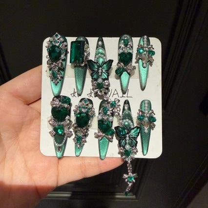 Handmade Emerald Green Cat Eye Long Stiletto Press On Nails. Luxury witchy false nails decorated with 3D green butterfly charms, large emerald crystals, pearls, silver rhinestones and dangling gem chains. Reusable fake nails for parties and cosplay.