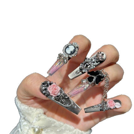 Handmade Metallic Silver Long Stiletto Press On Nails. Vintage gothic coquette false nails decorated with 3D pink roses, portrait cameo, black butterfly, pearls, silver rhinestones and dangling silver chains. Reusable fake nails for parties and cosplay.