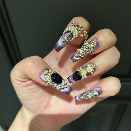 Handmade Purple Cat Eye Long Coffin Press On Nails. Dark royal gothic false nails decorated with large black heart & oval gems, vintage gold crown and cross charms, pearls, gold rhinestones and dangling gold chains