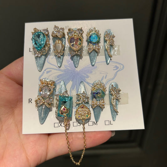 Silver Blue Cat Eye Stiletto Press-on Nails with Over-sized Blue Crystal Gems, Gold Bow, and Interlinked Hanging Chain - Luxury Glam Fake Nail Set