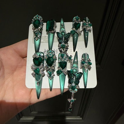 Handmade Emerald Green Cat Eye Long Stiletto Press On Nails. Luxury witchy false nails decorated with 3D green butterfly charms, large emerald crystals, pearls, silver rhinestones and dangling gem chains. Reusable fake nails for parties and cosplay.