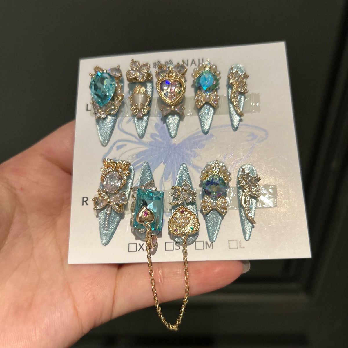 Silver Blue Cat Eye Stiletto Press-on Nails with Over-sized Blue Crystal Gems, Gold Bow, and Interlinked Hanging Chain - Luxury Glam Fake Nail Set