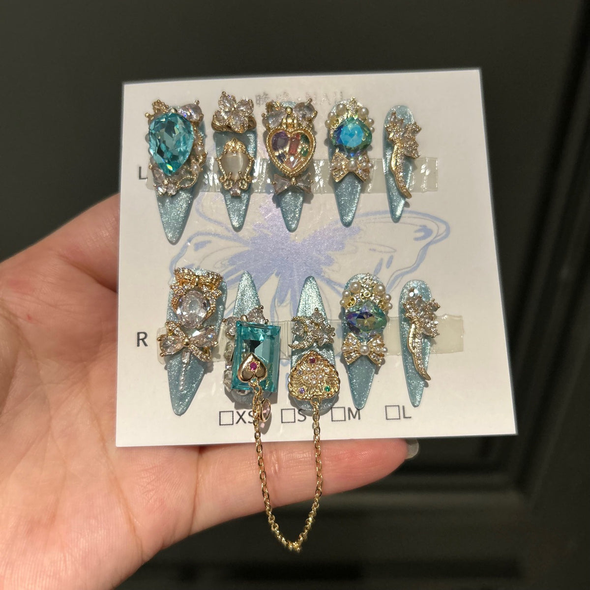 Silver Blue Cat Eye Stiletto Press-on Nails with Over-sized Blue Crystal Gems, Gold Bow, and Interlinked Hanging Chain - Luxury Glam Fake Nail Set