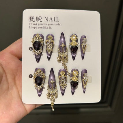 Handmade Purple Cat Eye Long Coffin Press On Nails. Dark royal gothic false nails decorated with large black heart & oval gems, vintage gold crown and cross charms, pearls, gold rhinestones and dangling gold chains