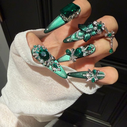 Handmade Emerald Green Cat Eye Long Stiletto Press On Nails. Luxury witchy false nails decorated with 3D green butterfly charms, large emerald crystals, pearls, silver rhinestones and dangling gem chains. Reusable fake nails for parties and cosplay.