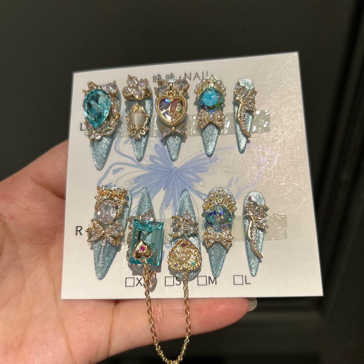 Silver Blue Cat Eye Stiletto Press-on Nails with Over-sized Blue Crystal Gems, Gold Bow, and Interlinked Hanging Chain - Luxury Glam Fake Nail Set