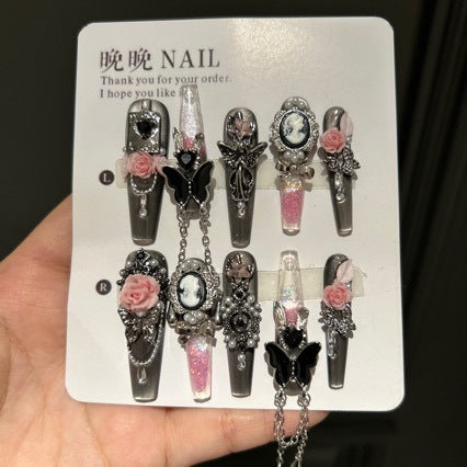 Handmade Metallic Silver Long Stiletto Press On Nails. Vintage gothic coquette false nails decorated with 3D pink roses, portrait cameo, black butterfly, pearls, silver rhinestones and dangling silver chains. Reusable fake nails for parties and cosplay.
