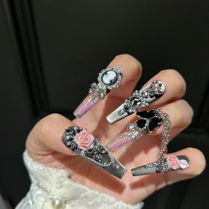 Handmade Metallic Silver Long Stiletto Press On Nails. Vintage gothic coquette false nails decorated with 3D pink roses, portrait cameo, black butterfly, pearls, silver rhinestones and dangling silver chains. Reusable fake nails for parties and cosplay.